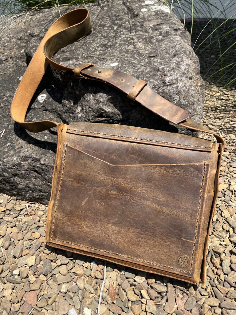 Handmade brown leather messenger bag photographed outdoors